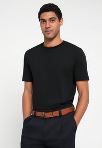 Fekete pamut póló rövid ujjakkal és kerek nyakkivágással, sötét nadrággal és fém díszítésű barna bőr övvel párosítva.