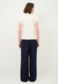 Weißes Oberteil mit kurzen Ärmeln, kombiniert mit lockeren, marineblauen Hosen. Glatter Stoff mit einem klaren, strukturierten Design und gerader Passform. Schlichter und moderner Look.