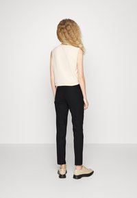 Un haut sans manches rose clair associé à un pantalon noir, avec une coupe ajustée. Des chaussures beige clair avec une semelle épaisse complètent la tenue.