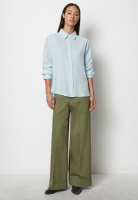 Himmelblaues Hemd mit Kragen und hochgerollten Ärmeln, kombiniert mit hochgeschnittenen, olivgrünen, weiten Hosen und schwarzen Ankle Boots.