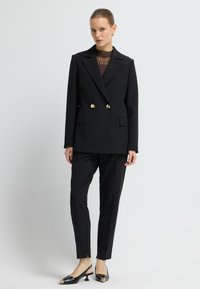 Zwart op maat gemaakt dubbelgeknopt blazer met gouden knopen, gecombineerd met bijpassende slim-fit broeken en puntige zwarte slingback schoenen met een gouden accent.