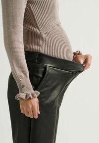 Schwarze Kunstlederhose mit breitem Bund, passend zu einem strukturierten, gerippten Blush-Pullover mit Rüschensäumen und metallischen Knöpfen.