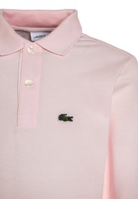 Lichtroze polo shirt gemaakt van textuurstof, met een kraag en drie knopen, en een groen geborduurd krokodillenlogo.