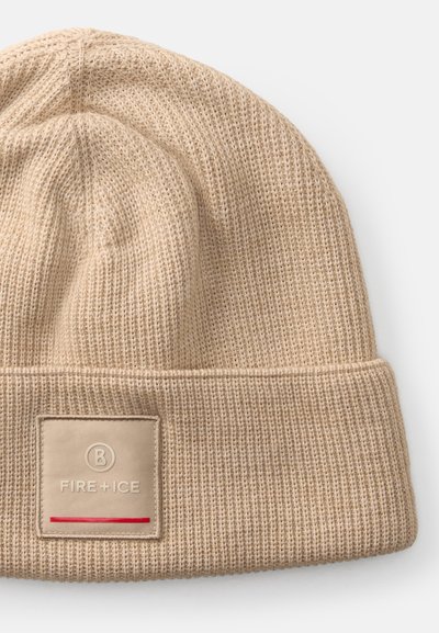 Gorro de punto beige con textura acanalada y un puño doblado. Presenta un parche cuadrado etiquetado "FIRE + ICE" con una línea de acento roja.