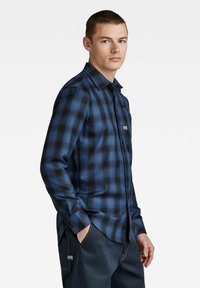 Blauwe en zwarte geruite blouse met lange mouwen, button-down kraag, borstzak en logo-opdruk aan de voorkant. Zachte stoftextuur, slim fit.