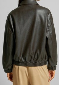 Brązowa skórzana kurtka o luźnym kroju, z prążkowanym dołem i kołnierzykiem. Gładka tekstura, elastyczne mankiety i prosty design.