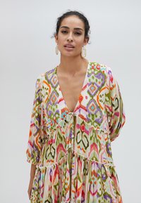 Flerfärgad maxiklänning med djup V-ringning, långa ärmar och lager på lager volangslut. Har intrikata geometriska och blommönster.