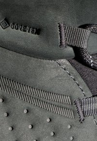 Dunkelgrauer GORE-TEX-Schuh mit strukturiertem Stoff, verstärkten Nähten und einer genoppten Optik, verfügt über ein elegantes Schnürsystem und horizontale Streifen.