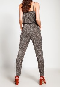 Jumpsuit senza maniche in stampa animale marrone e nera, con vita elasticizzata e gambe affusolate, abbinato a sandali con tacco rosso chunky.