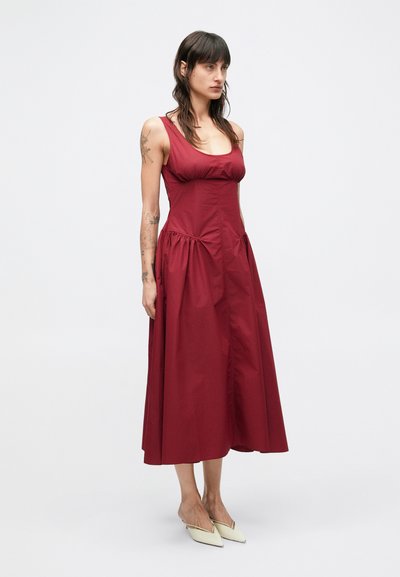 Φόρεμα μπόρντο χωρίς μανίκια με εφαρμοστό μπούστο, ραμμένες πλευρές και αέρινη φούστα. Λείο, ελαφρώς υφασμένο ύφασμα.