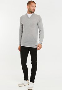 Jasnoszary sweter z dekoltem w serek i długimi rękawami, w połączeniu z czarnymi spodniami typu slim-fit i białymi trampkami z szarymi akcentami. Gładka tekstura.