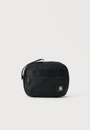Μικρή μαύρη ορθογώνια θήκη Carhartt με μπροστινή τσέπη με φερμουάρ και λουράκι καρπού σε απλό φωτεινό φόντο.