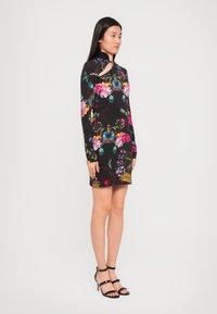 Zwarte lange mouw jurk met kleurrijke bloemenpatronen, sleutelgat halsdetail, textuurstof en een aansluitend ontwerp, gecombineerd met zwarte sleehak schoenen.