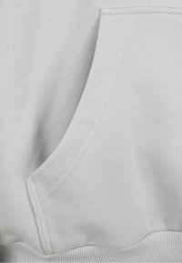 Sweatshirt gris clair avec poche kangourou à l'avant, tissu texturé et ourlet côtelé avec détails de coutures visibles.