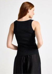 Black ribbed tank top with a fitted design, round neckline, and sleeveless style. Skin is visible on the back and shoulders.