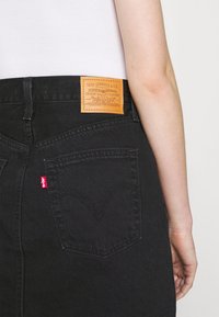 Jupe en denim noir avec une étiquette en cuir Levi Strauss & Co., une étiquette rouge sur la poche et des coutures courbes sur les poches arrière.