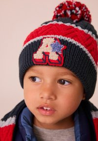 Knit beanie with a red, white, and navy design; features a textured knit, pom-pom top, and an "A" appliqué with a star accent.