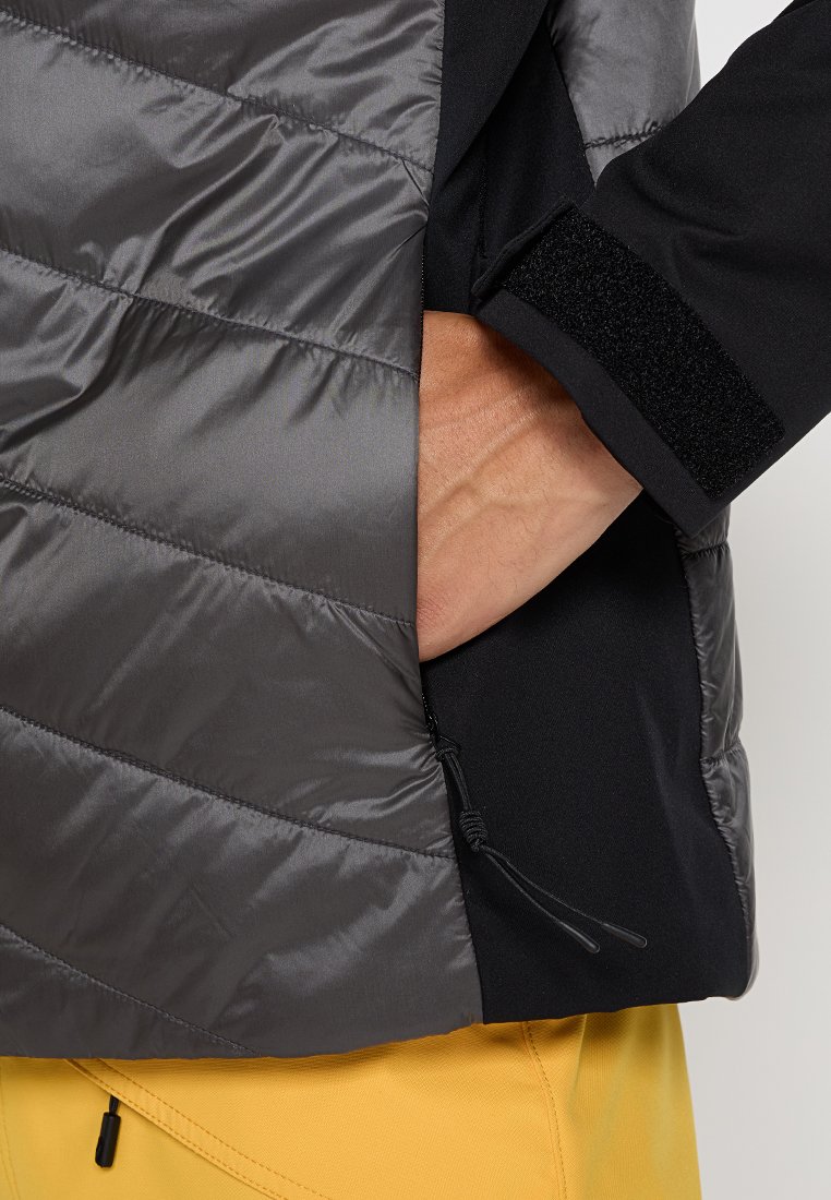 Grijze geïsoleerde jas met een doorgestikt ontwerp, voorzien van zwarte stofaccenten, een ritszak en een verstelbare drawstring aan de onderkant.