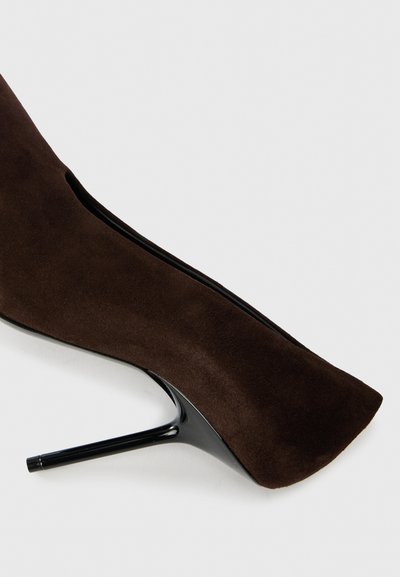 Brūni zābaki līdz potītei no zamšāda ar elegantu melnu stiletto papēdi un noapaļotu purngalu. Roku darbs izceltu dizainu gar sāniem.