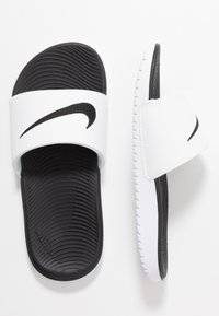 Valkoiset liukumäkipohjat mustalla kumipohjalla, leveä valkoinen hihna, jossa on musta Nike-swoosh-logo, ja uurteinen pohja.