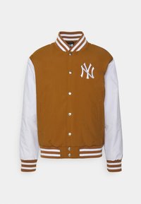 Brun och vit varsityjacka, med randig krage och handledsmuddar, tryckknappar och en vit broderad logotyp på bröstet.