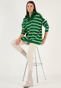 Groene en witte gestreepte oversized trui met een ritssluiting bij de kraag, gecombineerd met lichtbeige skinny pants en glanzende beige enkellaarsjes met een blokhak.