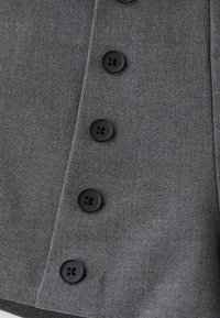 Gros plan d’un vêtement en tissu gris avec cinq boutons noirs à quatre trous espacés uniformément en rangée verticale.
