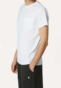 Hvid bomulds T-shirt med korte ærmer og en lomme på venstre bryst. Båret med sorte bukser, der viser en afslappet pasform og et enkelt design.