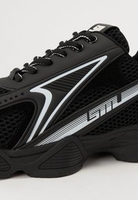 Black athletic shoe featuring a mesh upper, synthetic accents, reflective details, and a textured sole for grip and stability.