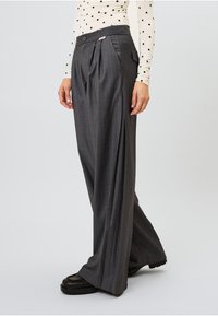 Pelēki šūti bikses ar svītrām, plecu priekšpuse, plakana jostasvieta un sānu kabatas. Nēsātas ar punktu rakstu topu un melnām kurpēm.