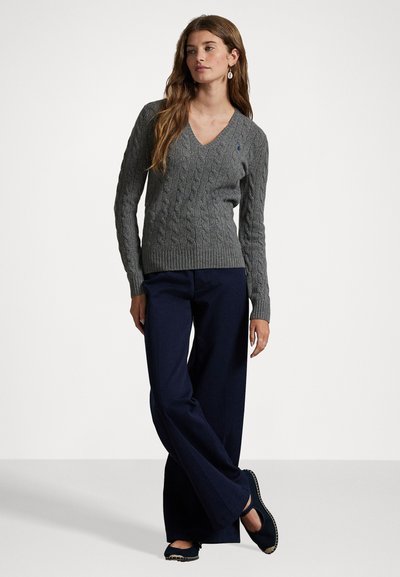 Γκρι πουλόβερ με λαιμόκοψη σε σχήμα V και πλέξη με καλώδιο, με ριμπ μανσέτες, σε συνδυασμό με σκούρο μπλε παντελόνι φαρδιάς γραμμής και μαύρα φλατ παπούτσια με διακοσμητικό στοιχείο.