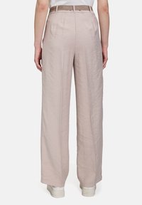 Světle růžové kalhoty s širokými nohavicemi, texturovaným povrchem a páskem v pase, s sklady vzadu a uvolněným střihem.