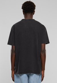 Sort bomulds t-shirt, afslappet pasform, korte ærmer, rund halsudskæring, synlige stikninger, slidte look, set fra ryggen.