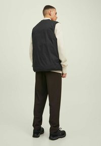 Chaleco negro sin mangas sobre un suéter claro, combinado con pantalones oscuros y zapatillas negras. El fondo es de un color neutro.