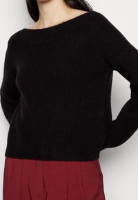 Czarny prążkowany sweter z szerokim dekoltem i długimi rękawami, zestawiony z wysokim, bordowym dołem. Miękka faktura, prosty fason.