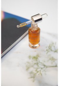 Amber glass dropper bottle with silver cap, containing a golden liquid. Placed beside a book on a marble surface with a flower sprig.