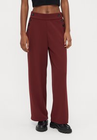 Pantalones de pierna ancha en color granate hechos de tela lisa, con una pretina alta y botones decorativos negros en el lateral.