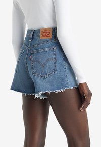 Shorts en denim avec un ourlet effiloché, de couleur bleu clair, et une étiquette en cuir Levi's sur la taille arrière. Présente deux poches arrière avec des accents de couture.