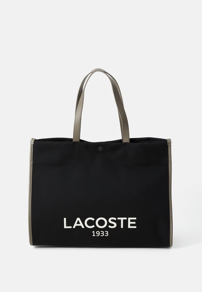 Borsa a spalla in tela nera con manici grigi, con logo bianco "LACOSTE 1933" sul davanti e chiusura a bottone sulla parte superiore.