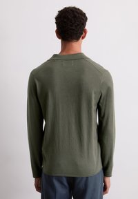 Polo à manches longues vert avec une texture douce, coupe décontractée et col. Présente un ourlet arrondi et des manches raglan.
