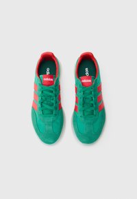 Rohelised ja punased spordijalatsid, mis on valmistatud seemisnahast ja võrgumaterjalist, millel on kolm punast triipu, polsterdatud krae ja tekstuuriga kummist tald.