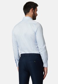 Jasnoniebieska koszula z klasycznym kołnierzykiem, zapinanymi na guziki mankietami oraz ciemnogranatowe spodnie o gładkiej fakturze z dwoma tylnymi kieszeniami.