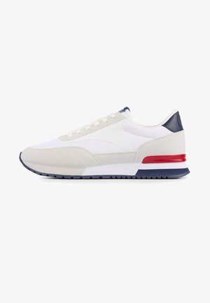White and beige sneaker with a textured upper, navy accents, red heel detail, and a ridged sole. Features a lace-up design.