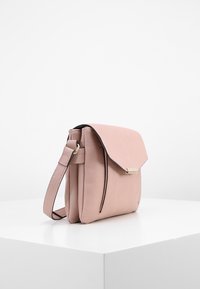 Borsa a tracolla in pelle rosa chiaro compatta con chiusura a pattina, fibbia dorata e tracolla regolabile, esposta su un piedistallo bianco.