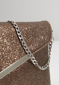 Sac en simili cuir brun texturé avec un éclat métallique, doté d'une anse chaîne argentée et d'un détail d'accent métallique élégant.