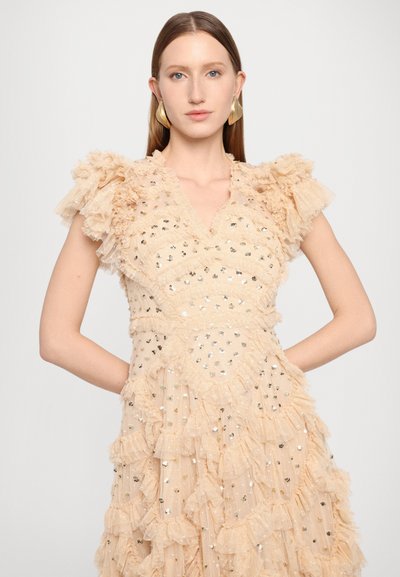Robe beige avec des manches à volants, ornée de paillettes argentées et dorées, avec des franges superposées et un décolleté en V.