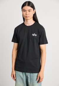 Schwarzes Baumwoll-T-Shirt mit kleinem weißem Logo auf der Brust. Klassisches Rundhalsdesign mit kurzen Ärmeln, lockerer Passform und glatter Textur.