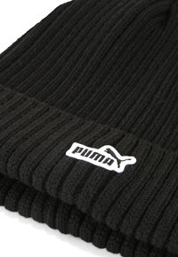 Berretto nero a maglia con texture a coste, orlo piegato e etichetta bianca del logo Puma sul lato. Il materiale appare morbido e caldo.