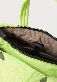 Φωτεινό πράσινο κουβερταρισμένο τσάντα με μαύρο φερμουάρ μερικώς ανοιχτό, αποκαλύπτοντας καφέ εσωτερική επένδυση και επενδεδυμένες λαβές.