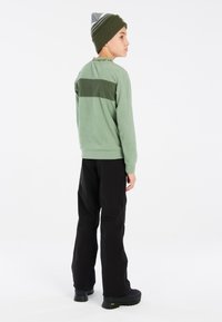 Žalias vilnonis megztinis su tamsiai žaliu horizontaliu raštu, derinamas su juodomis kelnėmis ir kepure, kuri turi pilkų ir žalių akcentų, ant vaiko.